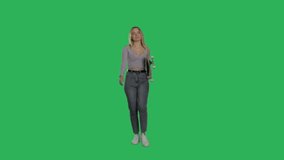 Young positive woman walking isolated on green screen background at studio . Blonde female dressed in casual clothes holding skateboard. Chroma key. 4k raw footage video front view