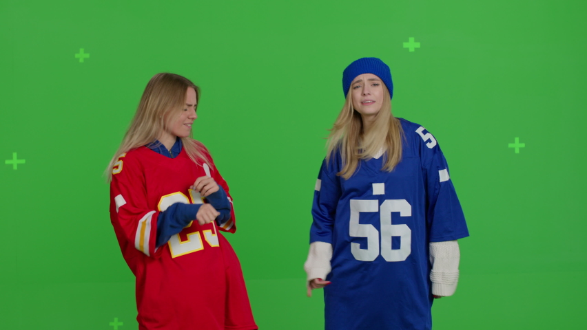 Two fan girls wearing color football t-shirts dancing . Young women in casual clothes having fun over green screen background. Chroma key