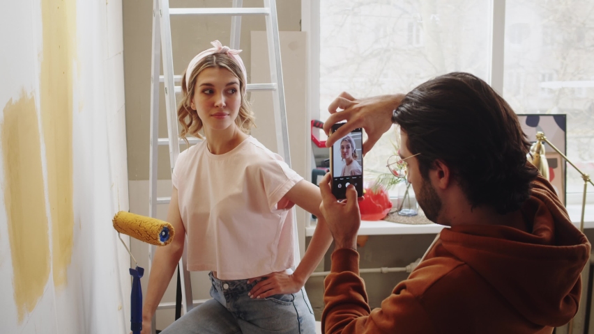 Young couple man and woman painting walls in yellow and taking photos on smartphone while making overhaul. Husband and wife doing renovating together. Interior design, new apartment.  Royalty-Free Stock Footage #1085142227