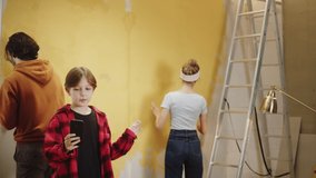 Family painting walls in yellow. Making overhaul together with child. Husband and wife doing renovating, son blogger recording video on smartphone, having fun. Interior design, new apartment. 