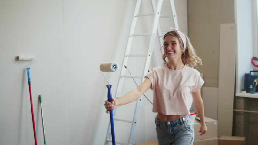 Woman singing and holding paint roller, female designer dancing, having fun. Happy housewife making overhaul, home renovating, painting walls. Smiling young wife during major maintenance.  Royalty-Free Stock Footage #1085142311