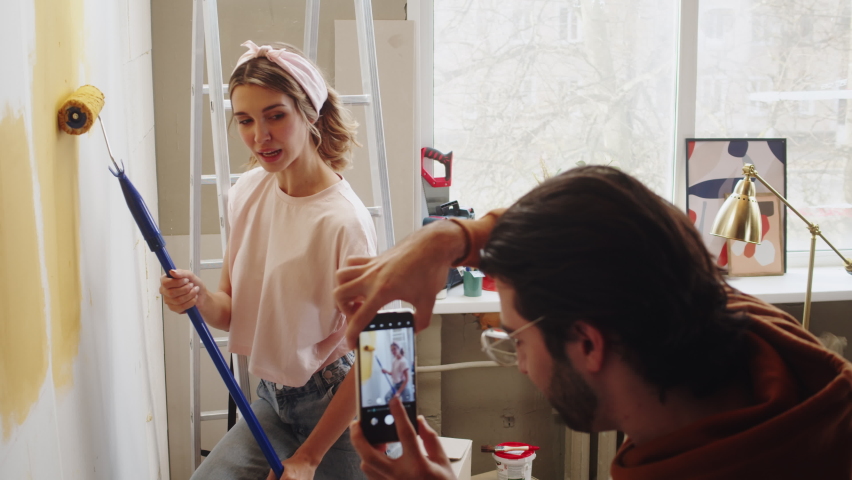 Young couple man and woman painting walls in yellow and taking photos on smartphone while making overhaul. Husband and wife doing renovating together. Interior design, new apartment.  Royalty-Free Stock Footage #1085142416