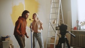 Young couple dancing while making overhaul, recording video about renovating and painting walls together. Man and woman making vlog about interior design, new apartment, having fun.
