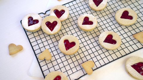Video of heart shaped Linzer cookies arranged on a black cooling rack against a white background. Love, romance and valentines food concept.