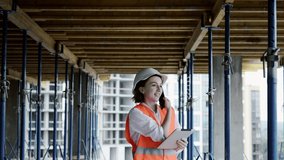 Young female civil engineer in safety jacket and helmet is talking on mobile phone on development construction site outdoor while working on laptop. - Powered by Shutterstock - Get 15% off with code: PIKWIZARD15