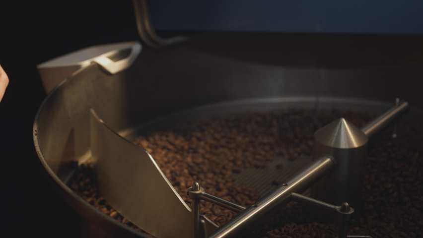 Roasting beans. A professional industrial roaster rotates organic coffee beans. The barista takes the hot aromatic coffee with his hand, checks the roast, mixes the beans. Slow motion Royalty-Free Stock Footage #1085146322