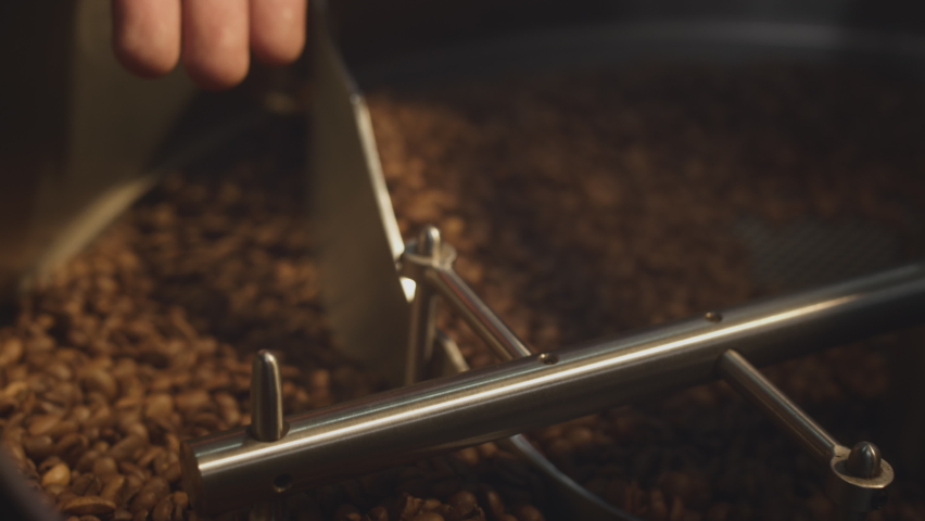 Roasting beans. A professional industrial roaster rotates organic coffee beans. The barista takes the hot aromatic coffee with his hand, checks the roast, mixes the beans. Slow motion Royalty-Free Stock Footage #1085146361