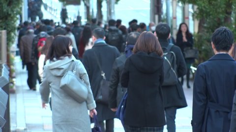 TOKYO, JAPAN : Crowd of people walking down the street in busy morning rush hour. Many commuters going to work in winter season. Japanese business, job and lifestyle concept. Slow motion, back shot.
