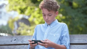 Young boy playing game on his smartphone outdoors in summer park. Addiction from electronic gadgets concept