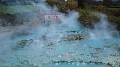 Flying through fog at the thermal hot springs bath and waterfall at Saturnia, Tuscany Italy close to Siena and Grosseto. Aerial drone at geothermal Cascate del Mulino, famous place near Monte Amiata.