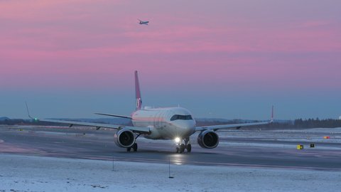 Oslo Airport Norway - December 16 2021: airplane taxiing at night very peri pantone sky colors another aircraft passing in air above oslo airport norway