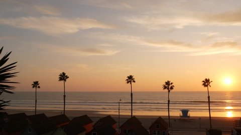 Palms silhouette sunset sky, California aesthetic. Oceanside USA. Tropical pacific ocean beach atmosphere. Los Angeles vibes. Lifeguard watchtower, palmtree and baywatch tower hut. Beachfront cottages