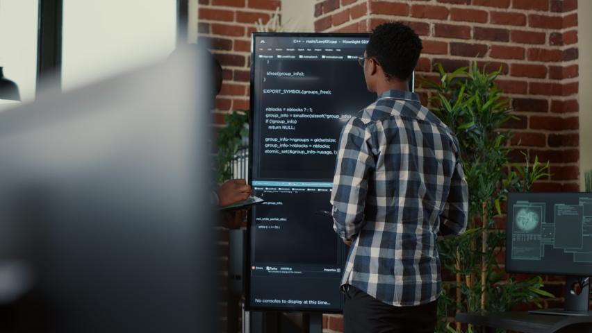 Team of software programmers leaving after analyzing source code on wall screen tv comparing errors using digital tablet. System engineers passing screens compiling code for artificial intelligence. Royalty-Free Stock Footage #1085169665
