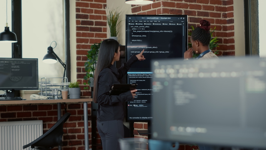 Software engineer holding digital tablet analyzing code on wall screen tv explaining errors to colleague programer in it startup office. Team of coders collaborating on ai innovation group project. | Shutterstock HD Video #1085169692