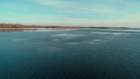 Aerial drone footag of flying over a calm river in winter forest in the distance