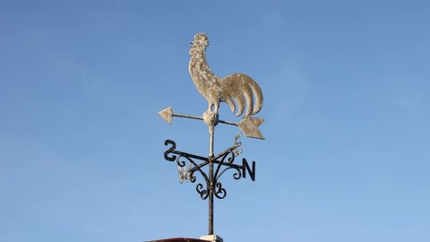 Isolated Cockerel Rooster weather vane moving in a light breeze against a blue sky. Aldeburgh, Suffolk, UK