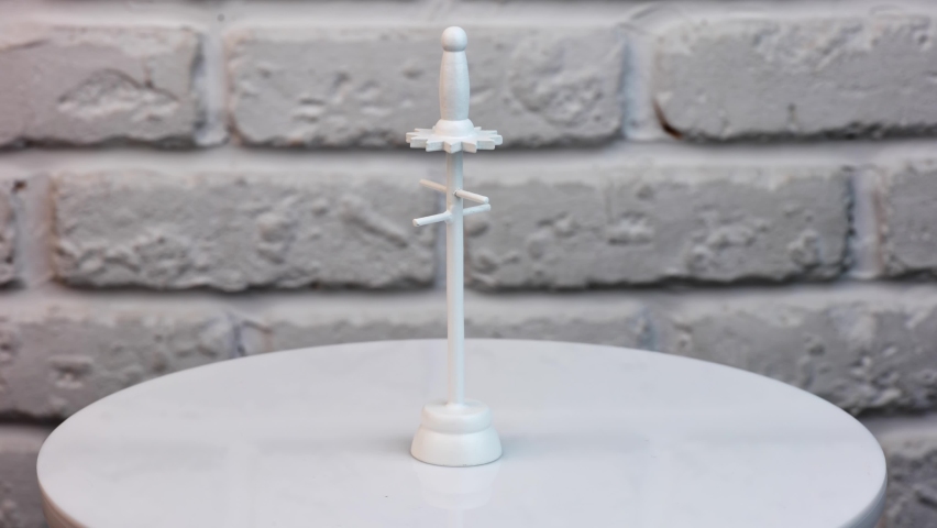 Miniature clothes rack made of wood. White hanger rotating at the table close up. White wall background.