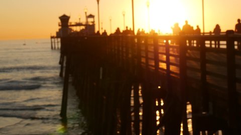 People walking, wooden pier in California USA. Oceanside waterfront vacations tourist resort. Ocean beach summertime sunset atmosphere. Blurred crowd strolling seaside boardwalk. Defocused seascape.
