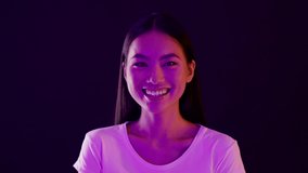Happiness Concept. Closeup Portrait Of Young Beautiful Asian Female Illuminated By Neon Light Laughing At Camera, Happy Korean Female Standing Under Purple Lighting Over Dark Background, Slow Motion