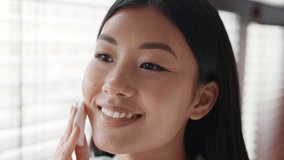 Facial Skincare. Happy Japanese Woman Using Cotton Pad Cleansing Skin And Removing Makeup In Modern Bathroom Indoor. Female Moisturizing Face With Lotion At Home. Slow Motion