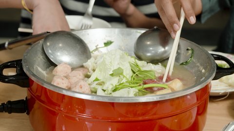 4K, The red sukiyaki pot had boiling water and the hand was putting vegetables and meat into the pot to prepare to eat.