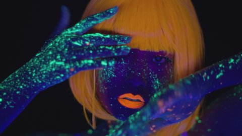 Nightlife and body art concept. Close up portrait of young fashionable asian lady with bright neon makeup dancing in fluorescent lights over black background