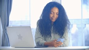 Young black businesswoman using mobile phone. Freelancer female browsing news feed on social media app with happy smile. Cheerful person uses modern smartphone device for netoworking and communication