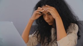 Depressed black woman. Stressed young adult female looking in laptop screen. Despairing African person thinking about problem solution in front of notebook computer at home