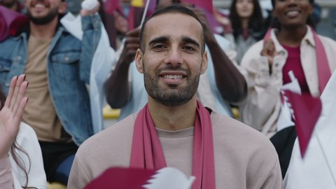 Portrait of happy arabian man looking at camera while sitting on tribune during football game. Dedicated fan supporting national team during world cup.