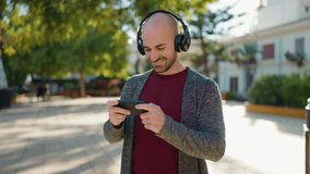 Young bald man smiling confident playing video game at park