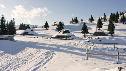 Parallax shot of Alpine, Wooden, Holiday Village, Small houses, huts, Chalets Covered with Snow, Standing On Peak of Hill With Rare Spruce Forest, Hills in The Background.