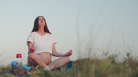 Pregnant woman meditates on hilltop sitting on yoga mat, front view. Pregnant woman is resting, meditating in open air