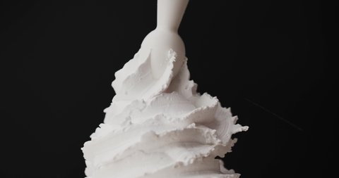 Squeeze whipped cream into spiral wave. Smooth whipped cream on black background. Slow - Motion , Food concept.