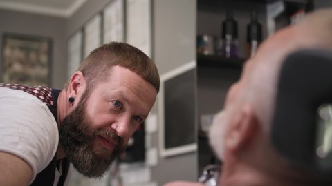 professional haircutter barber uses professional trimmer to trim beard and must-have old stylish man, close-up