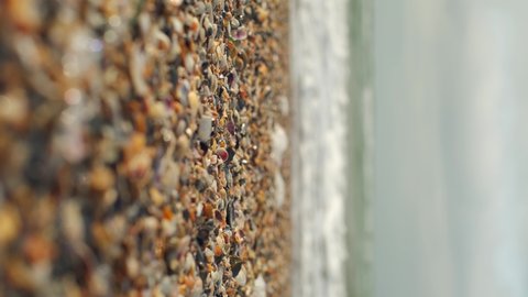 Shell beach, small seashells close-up on the beach and sea waves rolling along the shore. Beach vacation concept. Vertical footage. Selective focus. 4K video, place for text