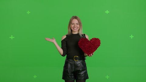 Happy caucasian girl with a hand-made paper heart in her hands expresses delight and joy , demonstrating love care on green screen background. Young woman pointing with hand . Valentine's Day