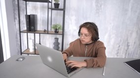 Portrait of a cute teenage girl having a video online lesson. A girl sits near a laptop with headphones and listens and writes. Happy young girl learn english language listen lecture