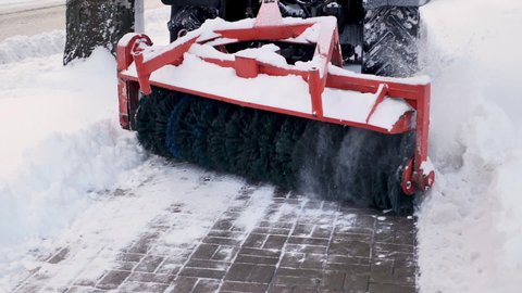 City service cleaning snow , a small tractor with a rotating brush clears a road in the city park from the fresh fallen snow on winter day