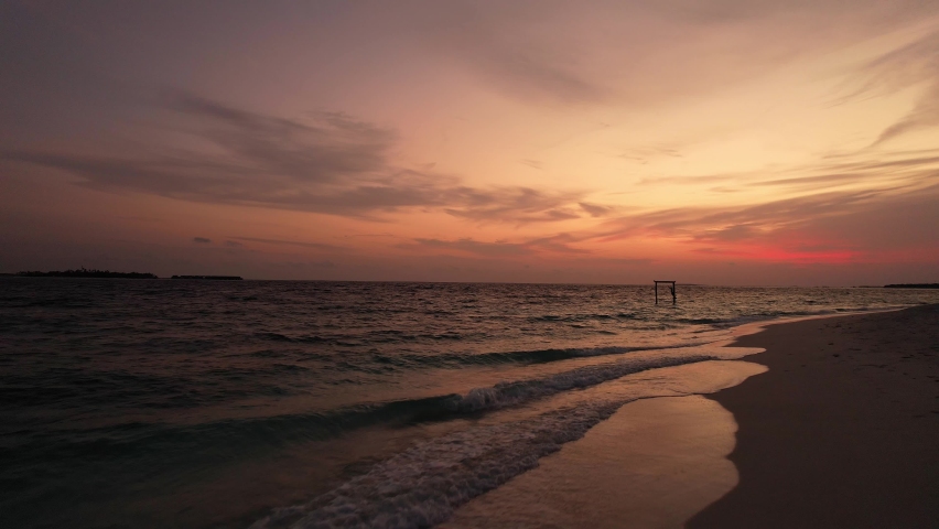 Drone shot fly over evening sea, orange sunset and person on a swing. Aerial shot of beautiful, panoramic view of ocean water and beach in Maldives. Concept of trip