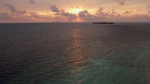 Aerial shot of picturesque sunset and small island in ocean. Beautiful, panoramic skyline of setting sun and calm water, beach in Maldives at night. Concept of trip
