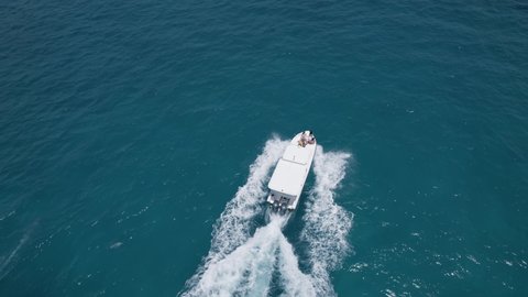 Top view of white boat with people moving, beautiful turquoise deep ocean texture. Aerial shot of blue waters and calm waves of Maldives island. Concept of tourism and travelling