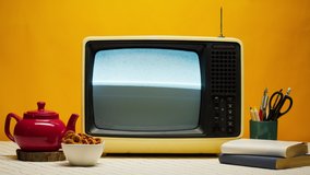 Close-up of old retro television on orange background. Broken TV with grey interference screen and antenna, red teapot on kitchen table, bad signal reception, cinematography concept.