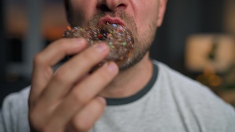 Man hastily eating sweet chocolate donut. Close-up