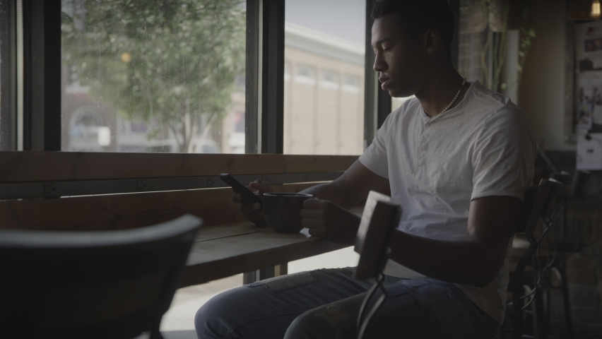 Man drinking in coffee shop surprised at cell phone social media - Provo, Utah, United States