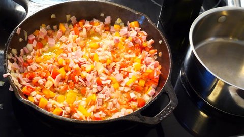 Tomatoes Ham Peppers and Onions Sizzling in Olive Oil in Cast Iron Frying Pan on Electric Glass top Stove