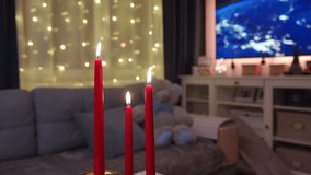 Living room interior with burning red candles on table and festive light chain on the window in the evening. High quality 4k footage