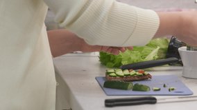 Woman cooking festive dinner in the kitchen making toast with cucumber and caviar. Bread topped with cream cheese, cucumber and salmon roe. High quality 4k footage