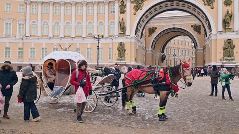 SAINT-PETERSBURG, RUSSIA - JANUARY 09 2022:  Horse-drawn  tourist carriage at a Palace Square and people walking around taking pictures  