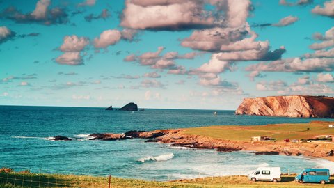 Time lapse of clouds moving over camper vans camping on Verdicio beach at Asturias coast in northern Spain. Cape Penas cliff in the distance. Travel with motor home.