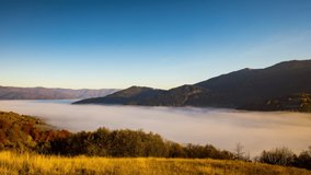 Thick morning fog fills highland deep valley among forestry mountains and hills slopes under clear blue sky at autumn sunrise 8K time-lapse video